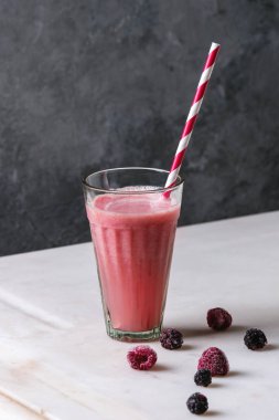 Kırmızı cam meyve buzlu karpuz kokteyl çizgili saman ile çilek ve dondurulmuş çilek arka plan, gri duvar beyaz mermer masada duruyor. Yaz soğuk içecek.