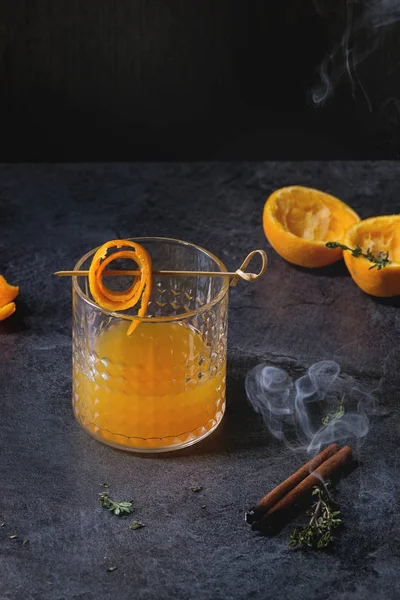 杯苏格兰威士忌橙汁酒精鸡尾酒与盘旋橙色果皮在串 百里香和抽烟肉桂棍子站立在黑大理石桌上 — 图库照片