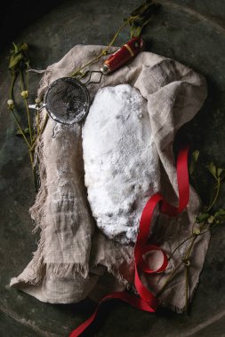 Tüm Christmas cake, geleneksel Alman şenlikli pişirme. Kepekli stollen kuru üzüm ve elek, kırmızı kurdele, eski karanlık metal arka plan üzerinde Ökseotu ile keten peçete üzerine pudra şekeri ile. Üstten görünüm