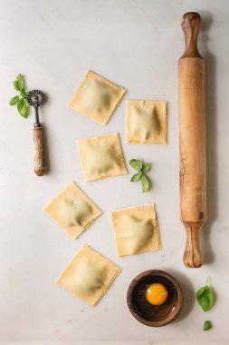 Ev yapımı çiğ çiğ İtalyan makarna Mantı personel ıspanak ricotta, yumurta sarısı, fesleğen, zeytin ahşap oklava. Beyaz mermer zemin. Düz lay, uzay