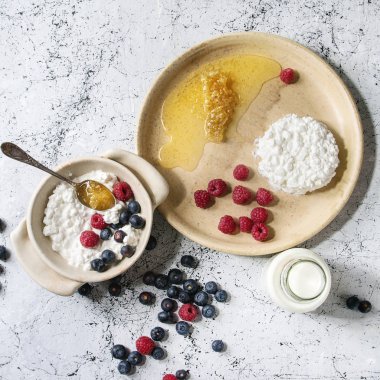 Ev yapımı peynir seramik kase beyaz mermer doku arka plan üzerinde yaban mersini, ahududu, şişe süt ve peteğin ile görev yaptı. Üstten görünüm alanı. Kare görüntüleri