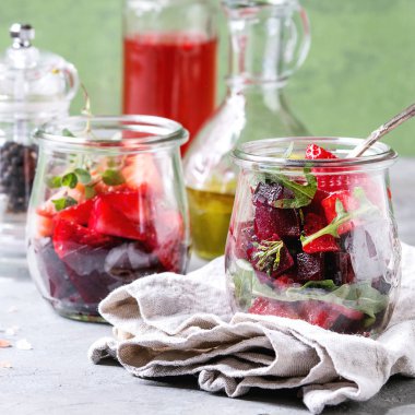 Pancar ve çilek salatası roka ve bez, biber ve şişe meyve ocet ve zeytin yağı ile cam kavanozlara fındık ile yeşil duvar ile gri tablo üzerinde arka plan olarak görev yaptı. Kare görüntü