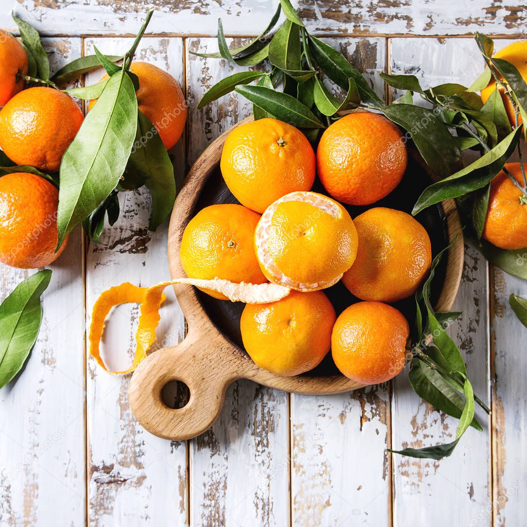 Ripe organic clementines or tangerines with leaves on wood serving board over white wooden plank table as background. Top view, space. Healthy eating. Square images