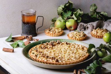 Ev yapımı tatlı elmalı kurabiye tart yeşil seramik tabak, mini tartlets ve sıcak çay vintage Kupası tutucu tarçın ile sopa, ceviz, elma dallarda beyaz mermer tablo yukarıda. Pişirme sonbahar.