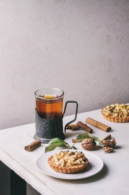 Ev yapımı tatlı elma kurabiye tartı beyaz plaka tarçın, ceviz, elma ile vintage Kupası sahibi sıcak çay bardak beyaz mermer masaya yukarıda dalları. Pişirme sonbahar.