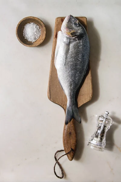 Raw uncooked gutted sea bream or dorado fish on wooden cutting board with ice, salt and pepper over white marble background. Flat lay, copy space. Cooking concept — Stock Image Raw Uncooked Gutted Sea Bream Dorado Fish Wooden Cutting Board Royalty Free Stock Images