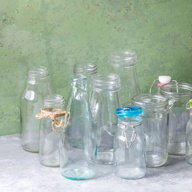 Farklı şekil boş açılan cam şişeler ve arka plan olarak yeşil duvar gri masada duran kapaklar olmadan çeşitli. Kare görüntü