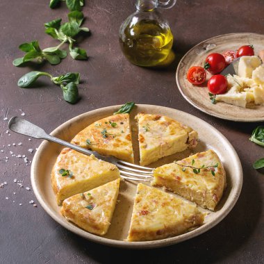 Seramik tabak içinde malzemelerle koyu kahverengi doku arka plan üzerinde hizmet pastırma ile İspanyol patates omlet tortilla dilimlenmiş. Kare görüntü