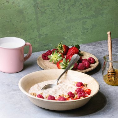 Tatlı pirinç lapası pudingi çilek çilek ve ahududu, ceviz, bal ve süt gri mutfak masasında arka plan olarak yeşil duvar ile bir fincan ile seramik plaka. Kare görüntü