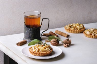 Ev yapımı tatlı elma kurabiye tartı beyaz plaka tarçın, ceviz, elma ile vintage Kupası sahibi sıcak çay bardak beyaz mermer masaya yukarıda dalları. Pişirme sonbahar.