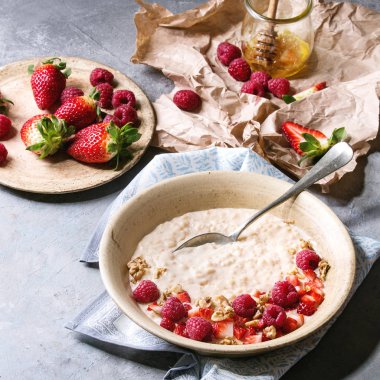 Tatlı pirinç lapası pudingi çilek çilek ve ahududu, ceviz, bal ve süt gri mutfak masasının üzerinde buruşuk Kağıt üzerinde bir fincan ile seramik plaka. Kare görüntü