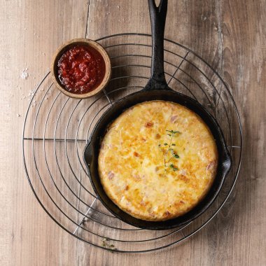 İspanyol patates omlet tortilla pastırma ile metal raf ahşap arka plan üzerinde soğutma domates soslu dökme demir tavada servis. Üstten görünüm alanı. Kare görüntü