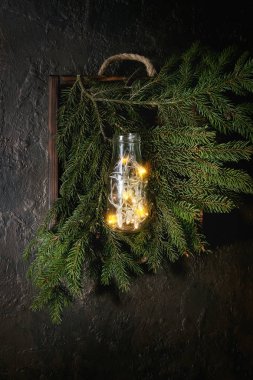 Noel çelenk karanlık doku arka plan üzerinde cam şişe yeşil çam ağacı dalları içinde ahşap tepsi üzerinde ışıklar. Noel tatil ruh kartı. Üstten Görünüm alanı ile
