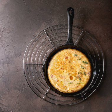İspanyol patates omlet tortilla pastırma ile dökme demir tavada raf koyu kahverengi doku arka plan üzerinde soğutma olarak görev yaptı. Üstten görünüm alanı. Kare görüntü