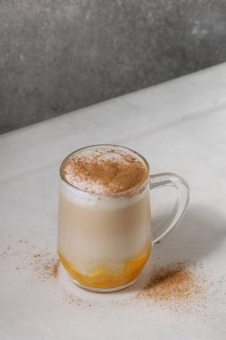Cam kabak spice latte kabak püresi, süt köpüğü ve arka plan, gri duvar beyaz mermer masada tarçın ayakta katmanlı. Kopya alanı