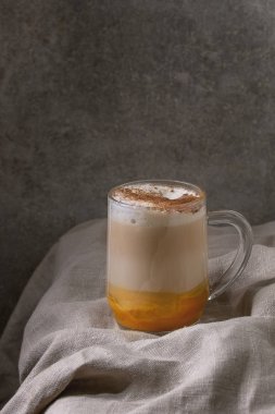 Cam kabak spice latte kabak püresi, süt köpüğü ve buruşuk masa örtüsü ile arka plan, gri duvar üzerinde tarçın duran katmanlı. Kopya alanı