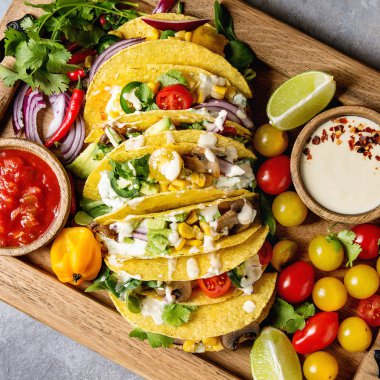 Çeşitli vejetaryen Mısır tacos, sebzeli biber domates ve malzemelerle krem soslar ile gri arka plan üzerinde ahşap tepsi üzerinde servis. Üstten görünüm alanı. Kare görüntü 