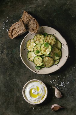 Kızarmış kabak salatası yoğurt sosu, sarımsak ve Çavdar ekmek dilimlenmiş seramik kaplamalar eski karanlık metal doku arka plan üzerinde gördüm. Vejetaryen yiyecekler. Düz lay, uzay
