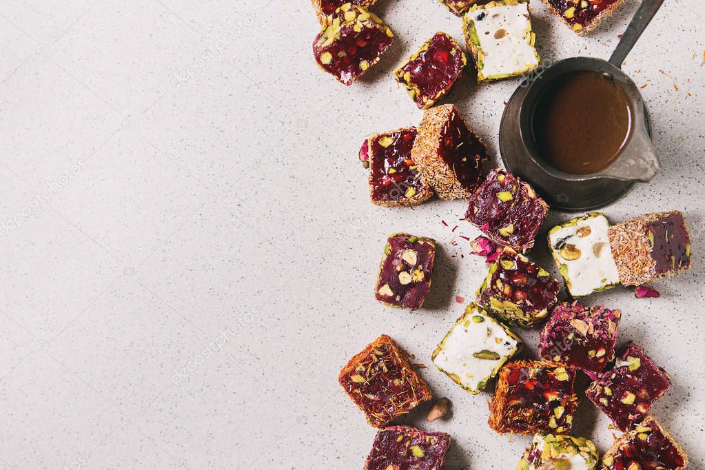 Variety of traditional turkish dessert Turkish Delight different taste and colors with rose petals and pistachio nuts, vintage coffee jezve over grey spotted background. Flat lay, copy space