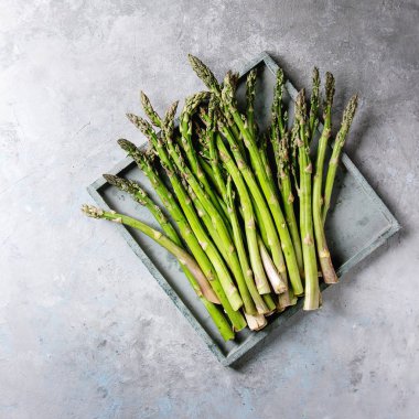 Çiğ çiğ organik yeşil kuşkonmaz içinde gri doku arka plan üzerinde ahşap tepsi. Görünümü en çok, uzay kopyalayın. Kare görüntü