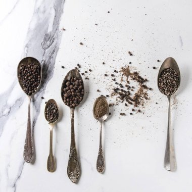 Farklı siyah biber yenibahar, yenibahar, uzun biber, rahipler biber, karabiber ve zemin toz beyaz mermer zemin üzerinde vintage kaşık içinde çeşididir. Üstten görünüm alanı. Kare görüntü