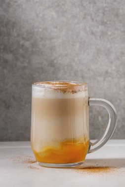 Cam kabak spice latte kabak püresi, süt köpüğü ve arka plan, gri duvar beyaz mermer masada tarçın ayakta katmanlı. Kopya alanı