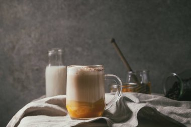 Cam kabak spice latte kabak püresi, süt köpüğü ve kavanoz ve buruşuk masa örtüsü ile arka plan, gri duvar üzerinde dekoratif beyaz kabaklar malzemelerle tarçın ayakta katmanlı.