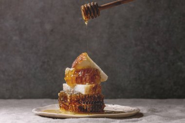 Organik bal peteğin ve ahşap kepçe akan baldan benekli seramik plaka keten masa örtüsü ile arka plan, gri duvar üzerinde buğday ekmek dilimleri için.