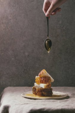 Peteğin ve benekli seramik plaka keten masa örtüsü ile arka plan, gri duvar üzerinde buğday ekmek dilimleri için kaşık akan bal organik bal.