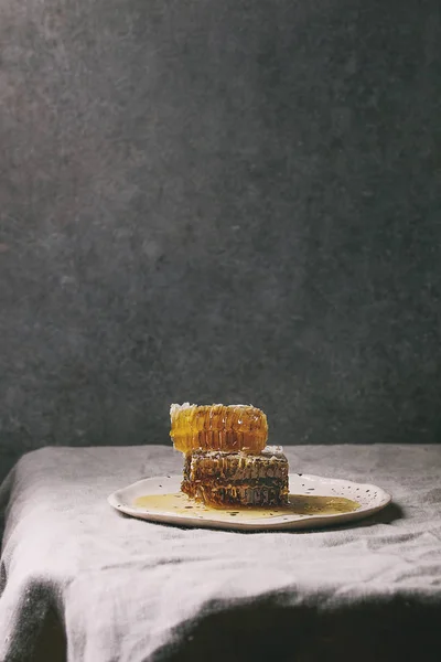 背景に灰色の壁とリネンのテーブル クロスに斑点を付けられたセラミック プレートにハニカム構造の有機蜂蜜 — ストック写真