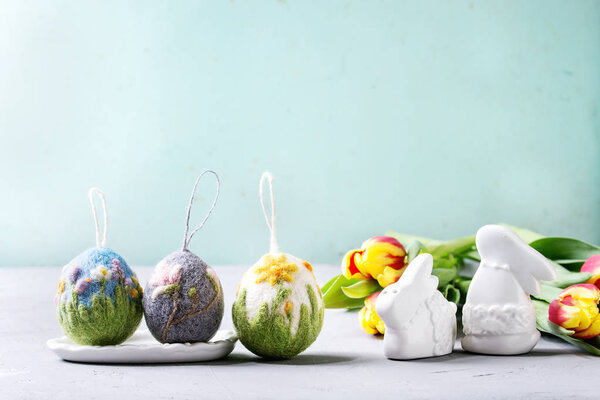 Set of craft felting Easter eggs with blooming flower poppies narcissus and magnolia and green grass decor standing on grey table. Easter decoration and gifts. Copy space
