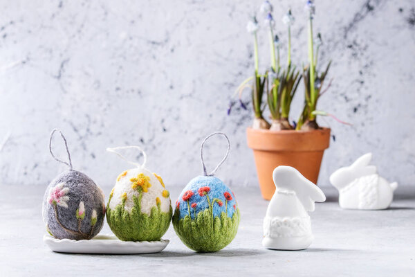Set of craft felting Easter eggs with blooming flower poppies narcissus and magnolia and green grass decor standing on grey table. Easter decoration and gifts. Copy space