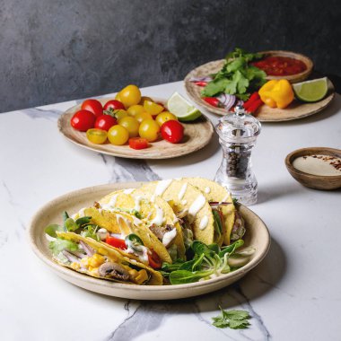 Çeşitli vejetaryen Mısır Tacos sebze, yeşil salata, biber biber domates ile seramik tabak ve beyaz mermer mutfak masasında malzemelerle krem soslar servis. Kare görüntü