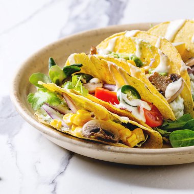 Domates ve beyaz mermer mutfak masasında krem soslar ile seramik plaka üzerinde çeşitli vejetaryen Mısır Tacos sebze, yeşil salata, biber ile servis. Yakın çekim. Kare görüntü