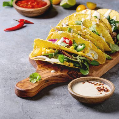 Vejetaryen Mısır Tacos sebze, yeşil salata, biber ile çeşitli soslar malzemelerle zeytin ahşap kesme tahtası üzerinde gri doku arka plan üzerinde servis. Kare görüntü