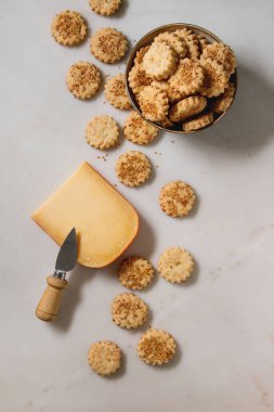 Ev yapımı Aperatif kurabiye peynir susam kurabiye kase ve beyaz mermer zemin üzerine bıçakla sert peynir parçası. Düz lay, uzay