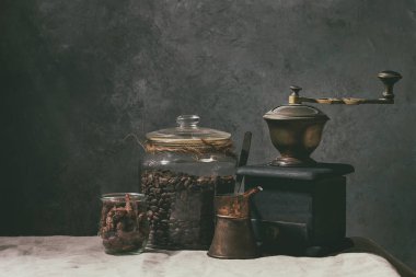 Kahve koleksiyonu. Kavanoz, vintage kahve değirmeni, jezve pot kavrulmuş siyah kahve çekirdekleri, tatlı badem ayakta keten masa örtüsü ile tabloda sekerli..