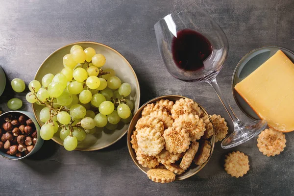 Wine snack. Cheese, grapes, nuts, cheese crackers cookies, honeycombs with laying glass of red wine and knife over dark texture background. Flat lay, space