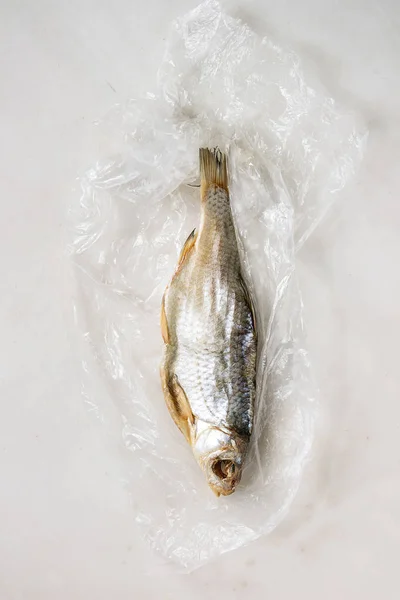 Dried fish or stockfish on plastic bag over white marble background. Flat lay, space — Stock Image Dried Fish Stockfish Plastic Bag White Marble Background Flat Lay Stock Photo