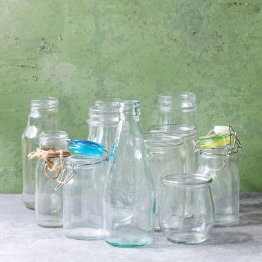 Farklı şekil boş açılan cam şişeler ve arka plan olarak yeşil duvar gri masada duran kapaklar olmadan çeşitli. Kare görüntü