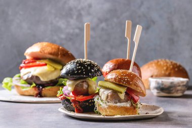 Çeşitli ev yapımı klasik ve mini hamburger buğday ve sığır ve Dana pirzola, eritilmiş peynir ve gri mavi tablo üzerinde beyaz seramik tahta sebze ile siyah buns.