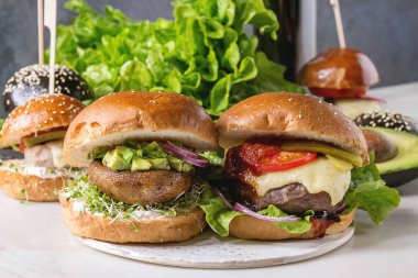 Çeşitli ev yapımı klasik, vegan ve mini hamburger buğday ve sığır ve Dana pirzola, portobello mantar, avokado beyaz mermer masa üzerinde beyaz seramik gemide ile siyah buns. Kola bir bardak ile.