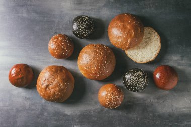 Ev yapımı geleneksel ve siyah mürekkep balığı mürekkep farklı boyut burger buns susam ile çeşitli bütün tohum ve mavi doku arka plan üzerinde dilimlenmiş. Düz lay, uzay