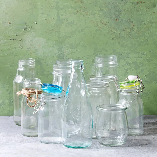 Farklı şekil boş açılan cam şişeler ve arka plan olarak yeşil duvar gri masada duran kapaklar olmadan çeşitli. Kare görüntü