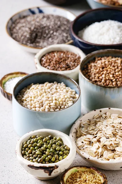 Variety of raw uncooked grains superfood cereal chia seeds, linen, sesame, mung bean, walnuts, tapioca, wheat, buckwheat, oatmeal, coconut, rice in ceramic bowls over grey spotted background. Close up — Stock Image Variety Raw Uncooked Grains Superfood Cereal Chia Seeds Linen Sesame Stock Image