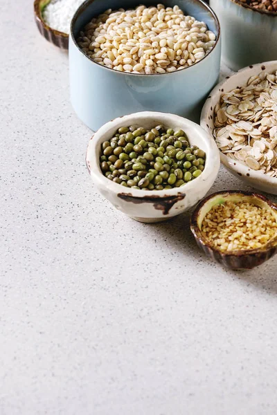 Variety of raw uncooked grains superfood cereal chia seeds, linen, sesame, mung bean, walnuts, tapioca, wheat, buckwheat, oatmeal, coconut, rice in ceramic bowls over grey background. Copy space — Stock Image Variety Raw Uncooked Grains Superfood Cereal Chia Seeds Linen Sesame Stock Image