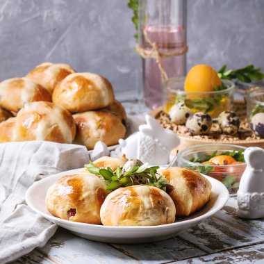 Turuncu yumurta Paskalya tablo ayarı renkli, tabak sıcak cross buns, yeşil dallar dekore edilmiş, cam Tekstil Masa örtüsü ile beyaz tahta ahşap masa üzerinde kokteyl içeceği. Kare görüntü