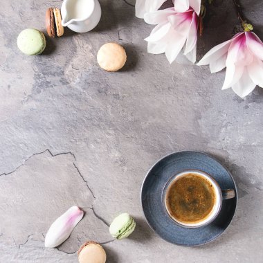 Mavi kupa siyah espresso ile Fransız tatlı macaroons kahve krema ve bahar çiçek Manolya dalları gri doku arka plan üzerinde. Üstten görünüm alanı. Bahar tebrik kartı. Kare görüntü