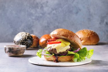 Çeşitli ev yapımı klasik ve mini hamburger buğday ve sığır ve Dana pirzola, eritilmiş peynir ve gri mavi tablo üzerinde beyaz seramik tahta sebze ile siyah buns.