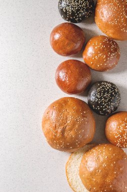 Ev yapımı geleneksel ve siyah mürekkep balığı mürekkep farklı boyut burger buns susam ile çeşitli bütün tohum ve beyaz benekli arka plan üzerinde dilimlenmiş. Düz lay, uzay